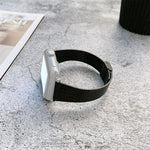 Buckle style steel replacement watchband for Apple Watch displayed on a gray surface with magazine and cup.