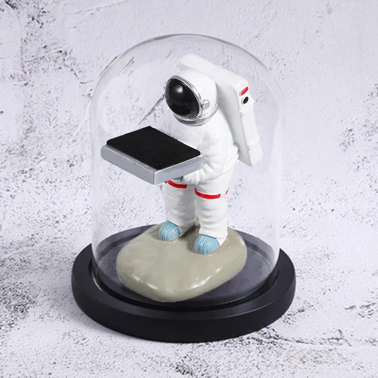 Decorative watch display stand featuring a small astronaut holding a black platform under a glass dome.